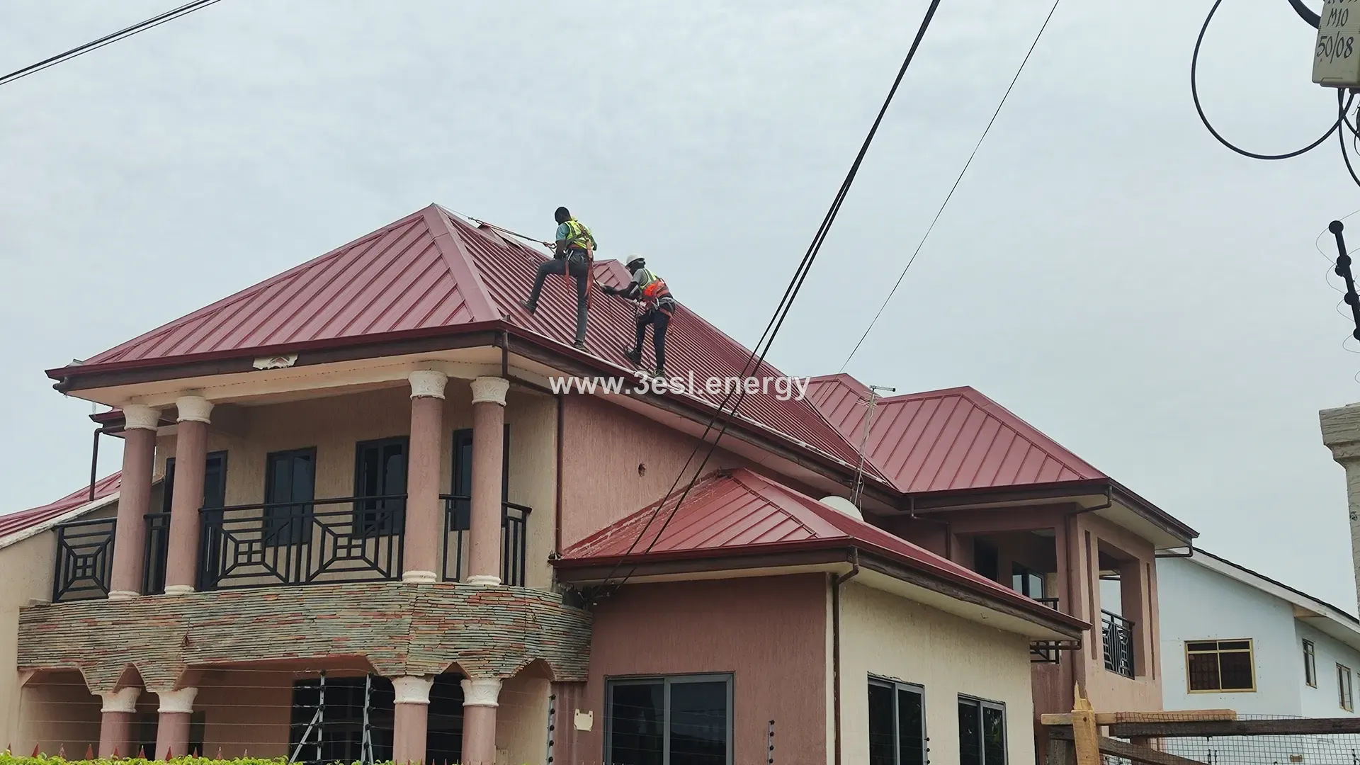 Two technicians working on the roof of a house alongside a partly completed solar array.