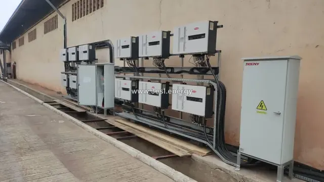 A long bank of industrial string inverters mounted along an external wall with cabling and combiner cabinets.