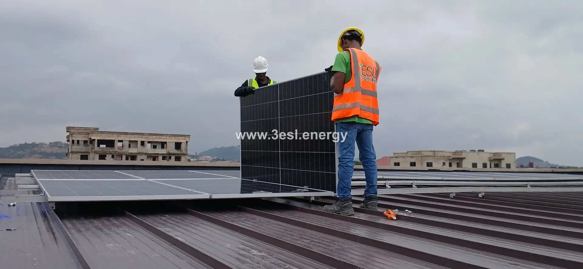 Two technicians in 3ESL vests carrying a photovoltaic module into position on a rooftop.